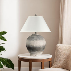 Betulla Table Lamp on a side table in a living room setting, featuring a gray base and white shade.