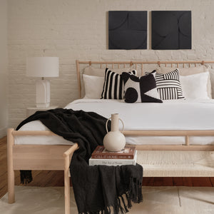 Mura wall decor displayed above a bed with black and white pillows in a cozy bedroom setting.