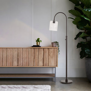 Danae floor lamp in a living room setting beside a wooden cabinet and plants.