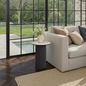 Alessio accent table beside a beige sofa in a bright room with large windows.