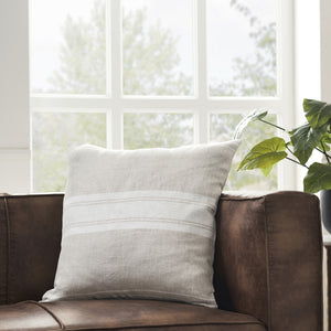 Raelyn Indoor Pillow on a brown leather couch, featuring light gray and white striped design.