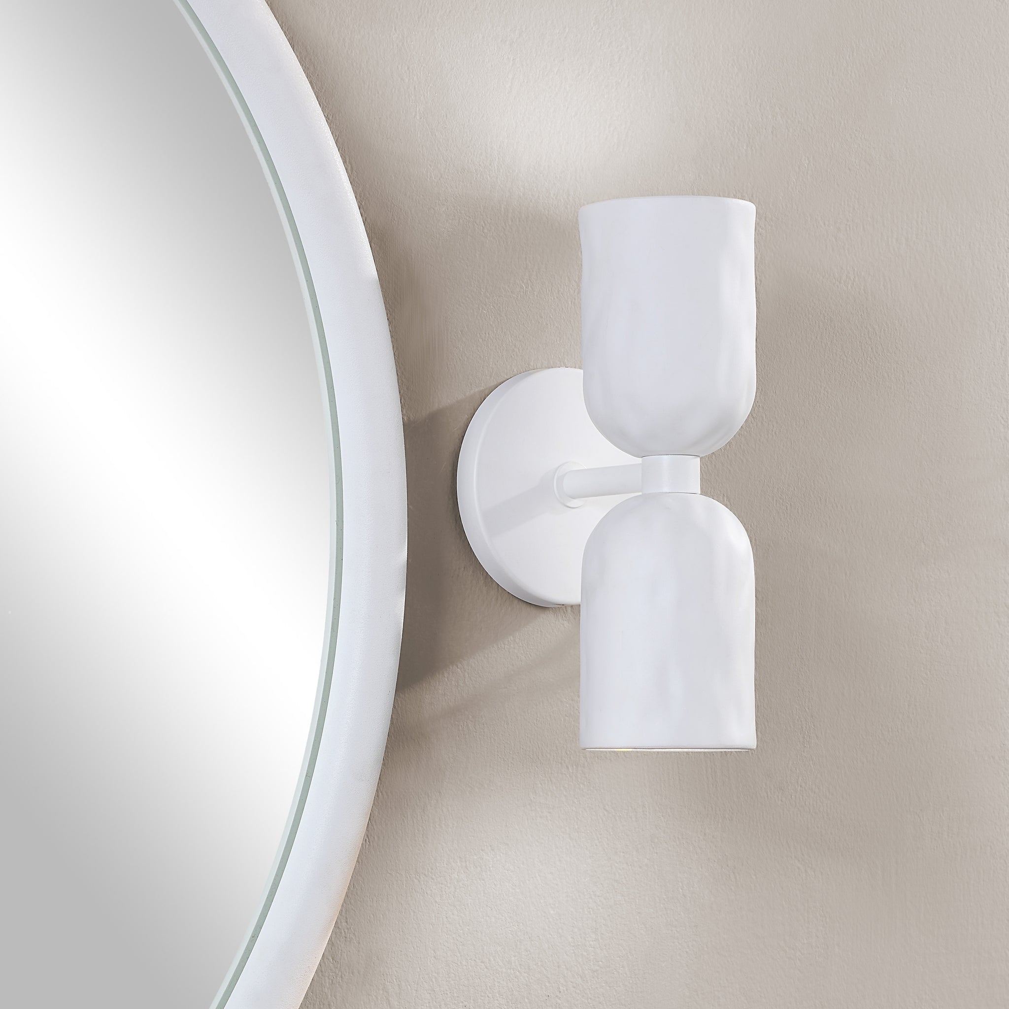Akira Wall Sconce in white mounted beside a round mirror on a textured wall