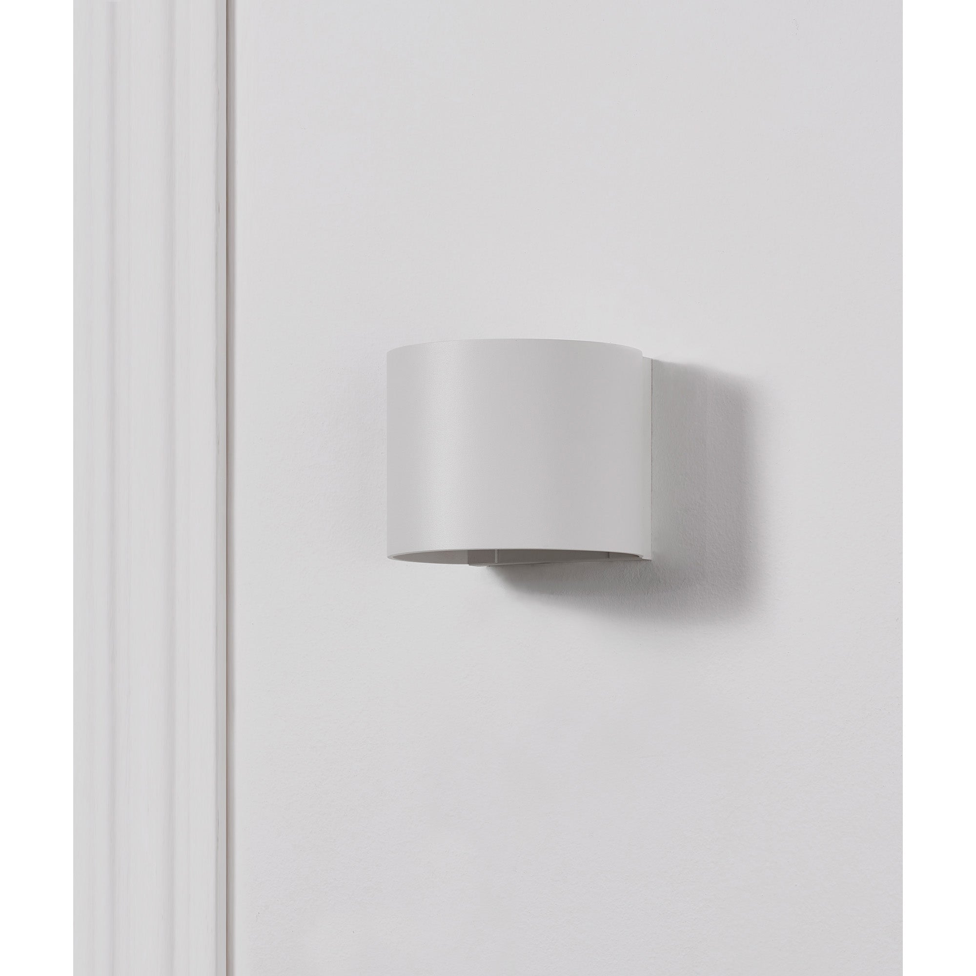 Zak Wall Sconce mounted on a white wall, featuring a simple cylindrical design.
