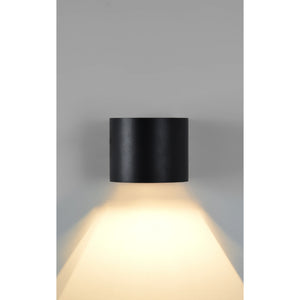 Lark Wall Sconce in matte black, casting light downwards with a sleek cylindrical shape.