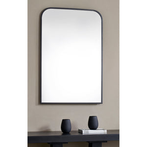 Jackline Wall Mirror displayed on a wall above a table with black vases and books.