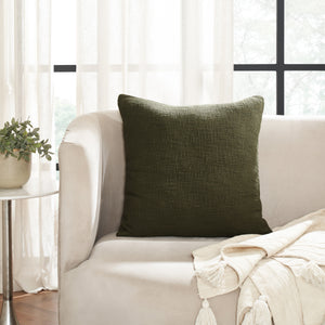 Sandro indoor pillow in dark green placed on a light-colored couch with a plant nearby.