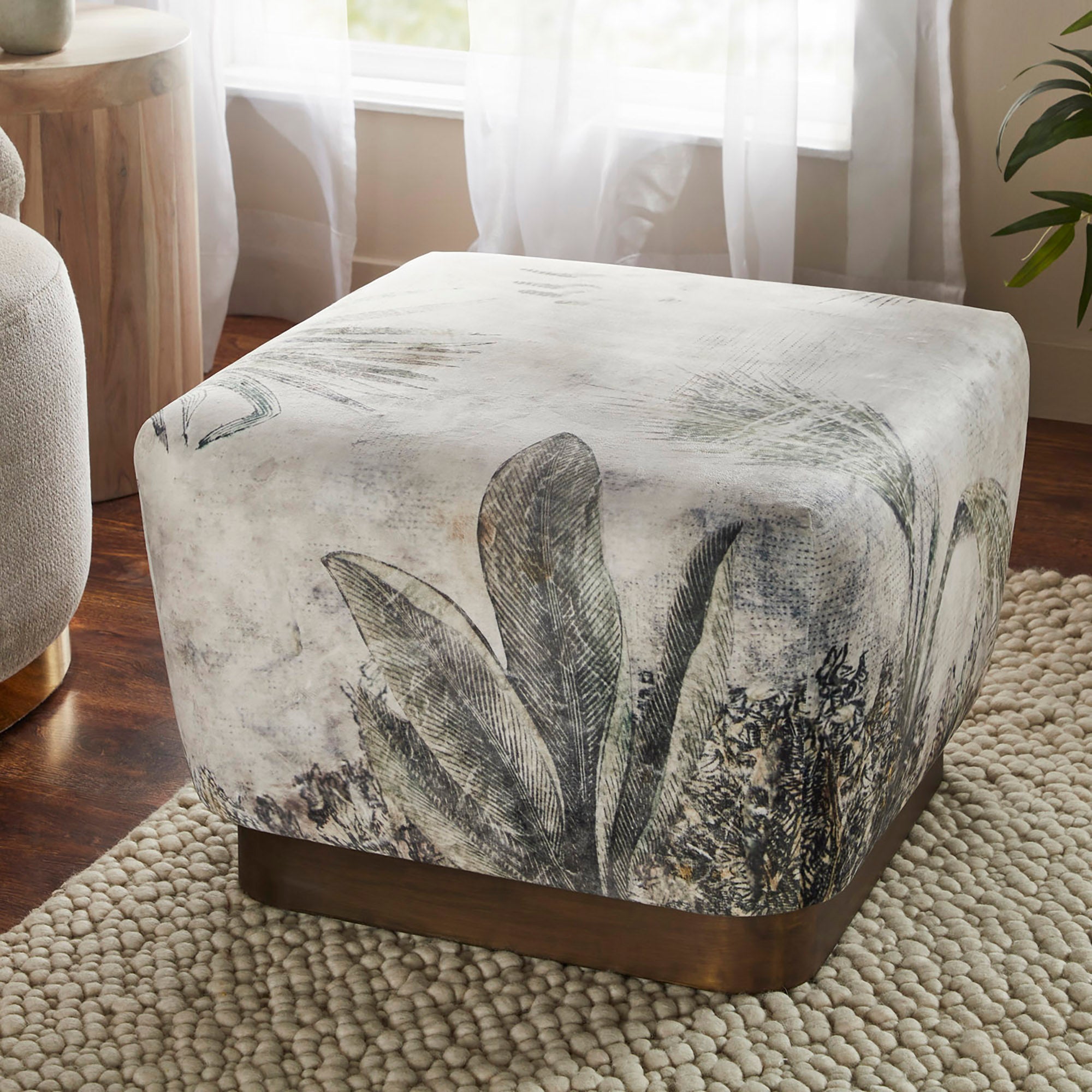 Tangle Ottoman in a living room setting, highlighting its floral fabric and wooden base.
