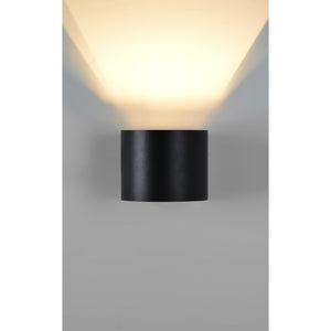 Lark Wall Sconce in matte black mounted on a wall, emitting warm light with a soft glow.