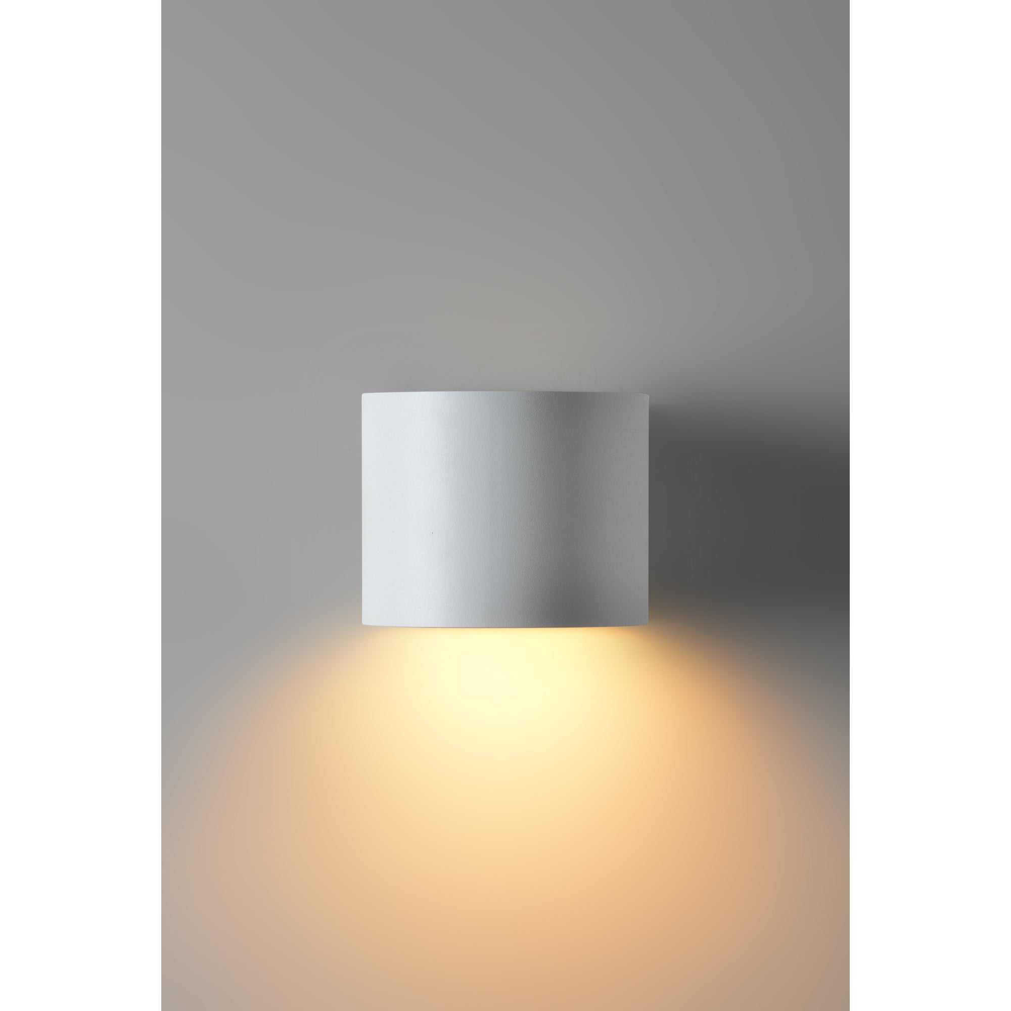 Zak Wall Sconce by Renwil, mounted on gray wall, emitting warm light downwards.