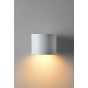 Zak Wall Sconce by Renwil, mounted on gray wall, emitting warm light downwards.