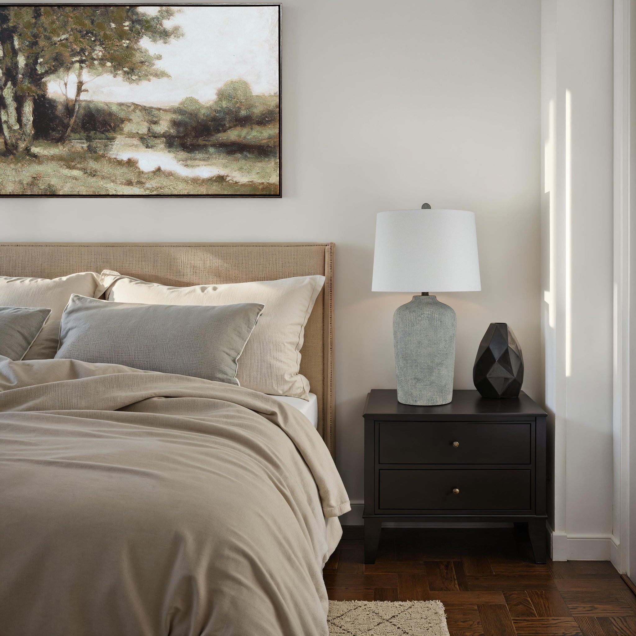 Aurelle table lamp on a nightstand beside a bed with neutral bedding and a decorative black vase.