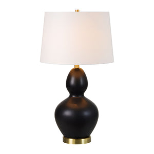 Kamilia Table Lamp illuminated, featuring a black ceramic body, white shade, and brass accents.