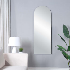 Mandra mirror with an arched top, mounted on a light gray wall, beside a white lamp and green plant.