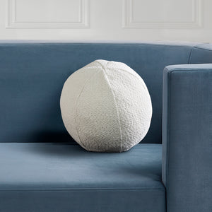 Solan Indoor Pillow in cream color placed on a blue couch, round shape, side view.